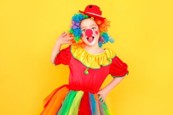 Portrait of girl clown, tongue out, looking at camera. Studio shot, isolated on yellow background